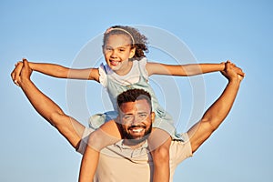 Happy loving father carrying his daughter on his shoulders while holding hands against blue sky. Adorable little girl on