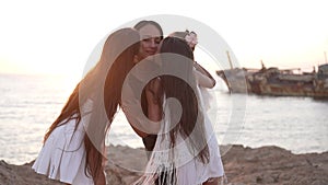 Happy loving girls kissing mother holding baby daughter standing in sunshine outdoors on sea beach. Cheerful Caucasian