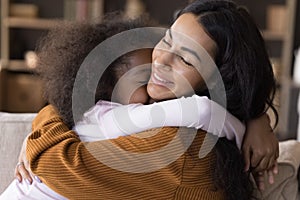 Happy loving kid cuddling smiling African American mother.