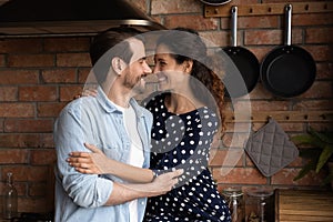 Happy loving millennial couple hugging, enjoying romantic moment in kitchen