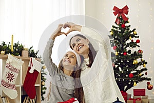 Happy loving mother and child celebrating Christmas and making heart symbol with hands