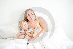 Happy and loving mother having fun and embrace her daughter on the bed. Family morning concept. Spending free time together at hom