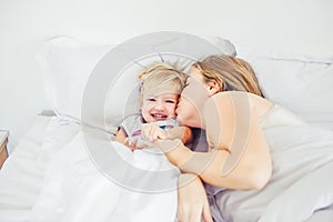 Happy and loving mother having fun and kissing her daughter on the bed. Family morning concept. Spending free time together at hom