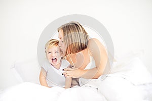 Happy and loving mother having fun and kissing her daughter on the bed. Family morning concept. Spending free time together at hom