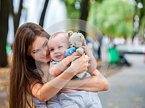 Happy loving mother and her baby outdoors with teady bear.