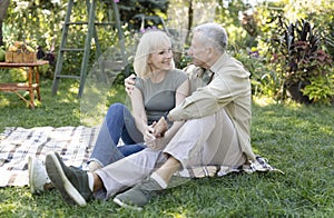 Happy loving senior couple having picnic in garden, embracing and smiling to each other, sitting together outdoors