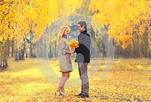 Happy loving young couple holding yellow maple leaves in autumn park on warm sunny day