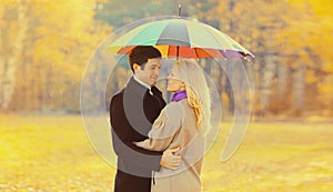 Happy loving young couple hugging under colorful umbrella in autumn park on warm sunny day