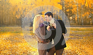 Happy loving young couple taking picture with film camera in autumn park on warm sunny day