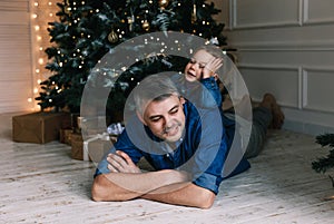 Happy loving young father lying on the floor playing with his little daughter near a decorated Christmas tree