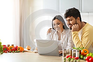 Happy loving young indian spouses using laptop while cooking