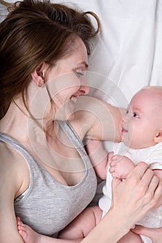 Happy loving young mother with her baby lying in bed. Portrait Top view