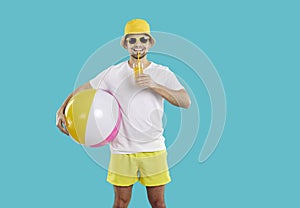 Happy male beach vacationer enjoys freshly squeezed orange juice isolated on light blue background.