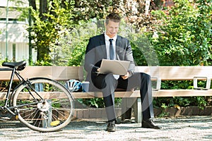 Businessman Sitting On Bench Using Laptop