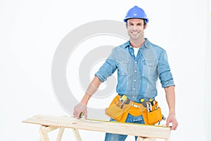 Happy male carpenter measuring wooden plank