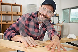 happy male carpenter sanding wood in workshop