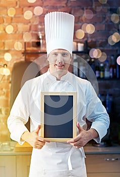 Happy male chef with blank menu board in kitchen