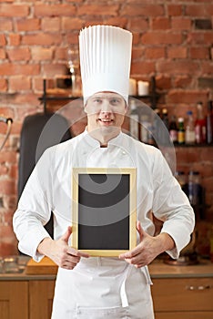 Happy male chef with blank menu board in kitchen