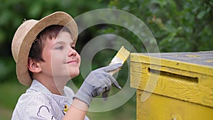 happy male child happily paints beehive with yellow paint while helping his grandfather beekeeper during holiday in