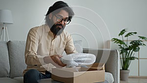 Happy male customer client consumer Arabian indian man guy in glasses open cardboard box at home unpack online shopping