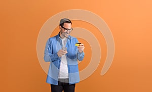 Happy male customer making online payment with mobile phone and credit card on orange background