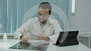 Happy male doctor working at office, writeing, smiling.