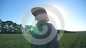 Happy male farmer in hat walking over green wheat field and enjoying nature. Young man going on cereal plantation and
