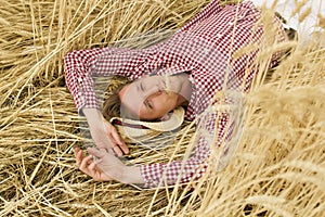 Happy male farmer laying on barley stalks and relaxing at barley meadow. Young agronomist lying on wheat stems and resting at