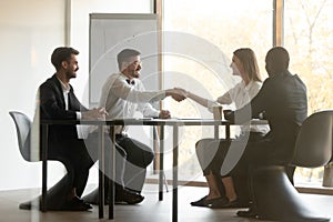 Happy male and female business partners handshake at group negotiation