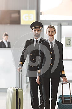 happy male and female pilots walking by airport lobby