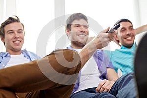 Happy male friends with remote watching tv at home