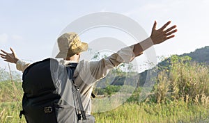 Happy male mountain hiker standing and looking at mountains with arms outstretched towards valley with blue sky.