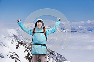 Happy male mountaineer man with raised arms. In background high mountains above clouds .