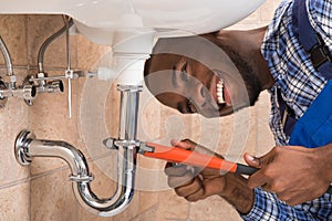Happy Male Plumber Repairing Sink In Bathroom