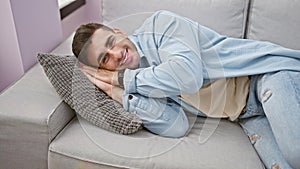 Happy male portrait, confident, handsome young hispanic man relaxing, resting on the cozy sofa indoors
