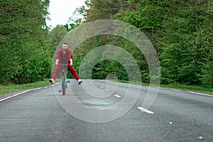 Happy male riding bike with legs up. The road in the forest. The concept of a healthy lifestyle, cardio training. Copyspace