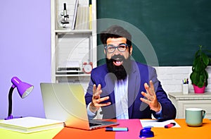 Happy male school teacher or university professor in classroom at desk. Bearded student man in glasses preparing for