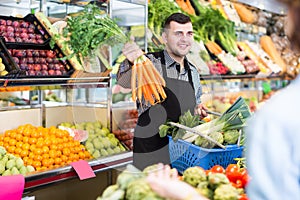 happy male shopping assistant helping customer to buy fruit and vegetables in grocery shop