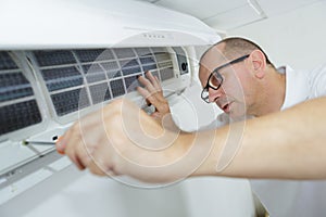 Happy male technician repairing air conditioner with screwdriver