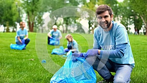 Happy male volunteer putting rubbish in garbage bag and smiling, responsibility
