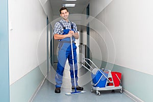 Happy male worker with broom cleaning office corridor