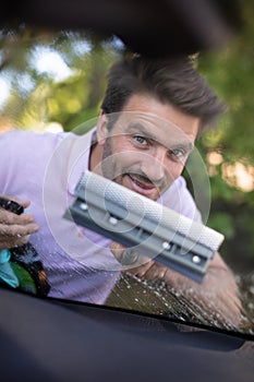 happy male worker cleaning car windshield