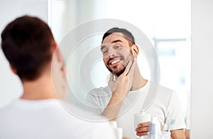 Happy man applying aftershave at bathroom mirror photo