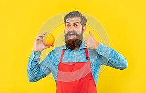 Happy man in apron giving thumb to fresh orange citrus fruit yellow background, fruiterer photo