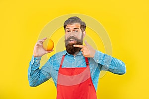 Happy man in apron pointing finger at fresh orange citrus fruit yellow background, fruiterer photo