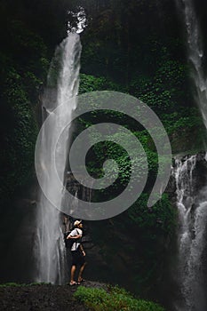 Happy man backpacker enjoying amazing tropical waterfall on background nature landscape. Travel Lifestyle and success