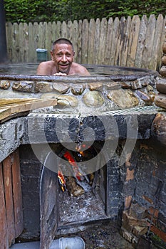 Happy man bathing in the cast iron vat with mineral water containing hydrogen sulphide. Water in cast iron vats heated to 40-45