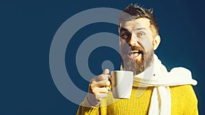 Happy man with beard in yellow sweater wrapped in white scarf with cup of hot coffee or tea. Handsome bearded man with