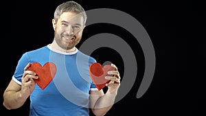 Happy man in blue tshirt holds two red heart shapes. Love, romance, dating, relationship concepts. Black background