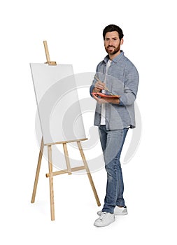 Happy man with brush and artist`s palette near easel with canvas against white background. Creative hobby
